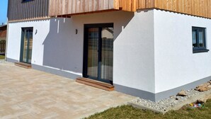 A modern two-story house with a wooden facade, large windows, and a covered patio area. - Apartment 'Ferien Bei Mari' with Mountain View, Private Garden and Wi-Fi (Schwangau)