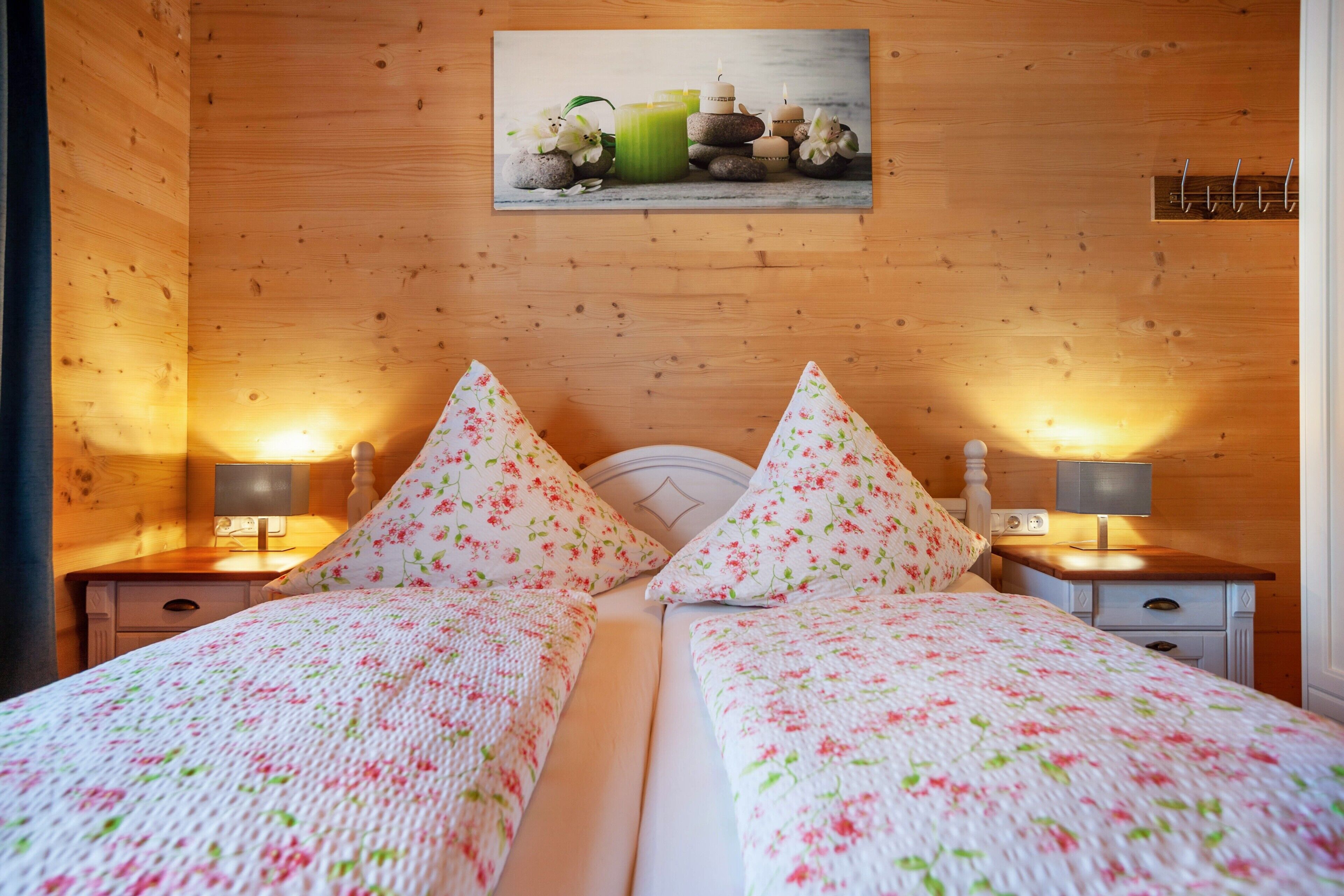 A double bed with floral bedding, two bedside lamps, a wooden headboard, and a wall-mounted picture.