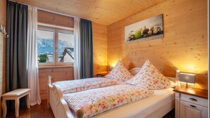 A wooden-paneled bedroom with a bed, a nightstand, a window with curtains, a bench, and a painting on the wall. - Apartment 'Ferien Bei Mari' with Mountain View, Private Garden and Wi-Fi (Schwangau)