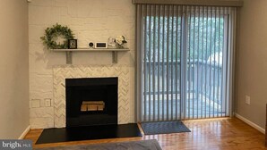 Un salon avec une cheminée, un plancher en bois, une porte-fenêtre coulissante et un mur en briques blanches.