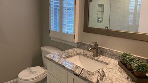 Une salle de bain avec des toilettes, un lavabo et une fenêtre équipée de stores.