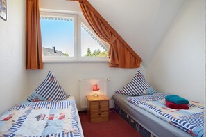 Une chambre avec deux lits simples, une table de chevet avec une lampe, une fenêtre avec des rideaux et un radiateur.