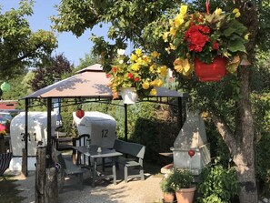 Un kiosque agrémenté d’une table et de chaises, entouré de plantes en pot et d’un arbre.