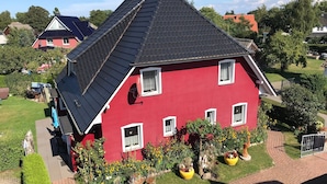 A red house with a sloped roof, solar panels, and a garden with flowers and chairs. - Apartment 'Fewo 32 - Halbinsel Darss - Ostsee' with Private Terrace, Shared Garden and Wi-Fi (Wieck am Darß)