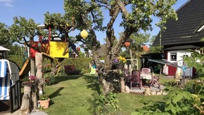 A garden with a play structure, a small table with chairs, and a red building in the background. - Apartment 'Fewo 32 - Halbinsel Darss - Ostsee' with Private Terrace, Shared Garden and Wi-Fi (Wieck am Darß)