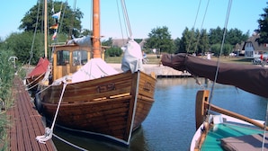 A wooden boat docked at a pier with a covered cabin and a flag. - Apartment 'Fewo 32 - Halbinsel Darss - Ostsee' with Private Terrace, Shared Garden and Wi-Fi (Wieck am Darß)