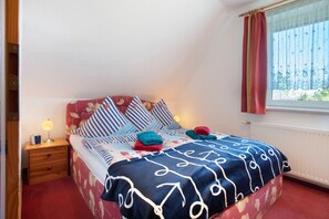 Une chambre à coucher avec un lit, une table de chevet, une fenêtre avec des rideaux et un radiateur.