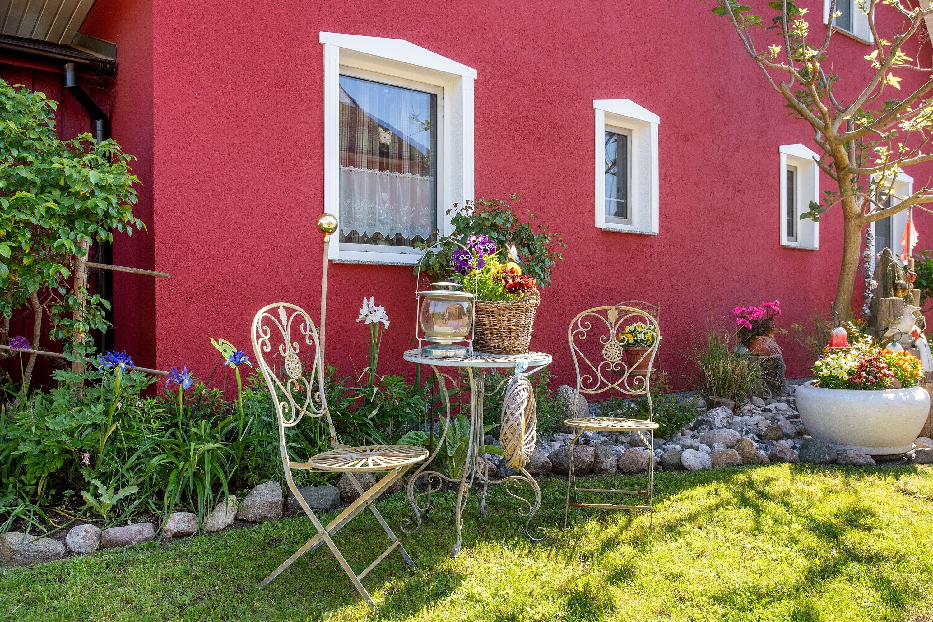 A red building with a garden, outdoor seating, and a large planter with flowers.