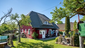 A red house with a sloped roof, a fenced yard, and a small patio area with outdoor furniture. - Apartment 'Fewo 33 - Halbinsel Darss - Ostsee' with Private Terrace, Shared Garden and Wi-Fi (Wieck am Darß)