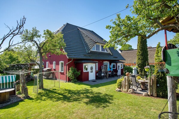Una casa roja con techo inclinado, patio cercado y un pequeño patio con muebles de exterior.