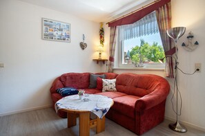 Ein Wohnzimmer mit einem roten Sofa, einem kleinen Holztisch, einer Stehlampe und einem Fenster mit Vorhängen.