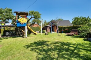 Ein Garten mit Spielhaus, Rutsche, Schaukel und einem kleinen Gartenhaus.