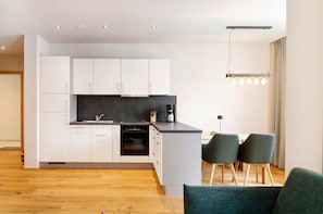 A modern kitchen with white cabinets, a black countertop, and a dining area with two chairs. - Apartment 'Pfrunger Ried' with Balcony and Wi-Fi (Herbertingen)