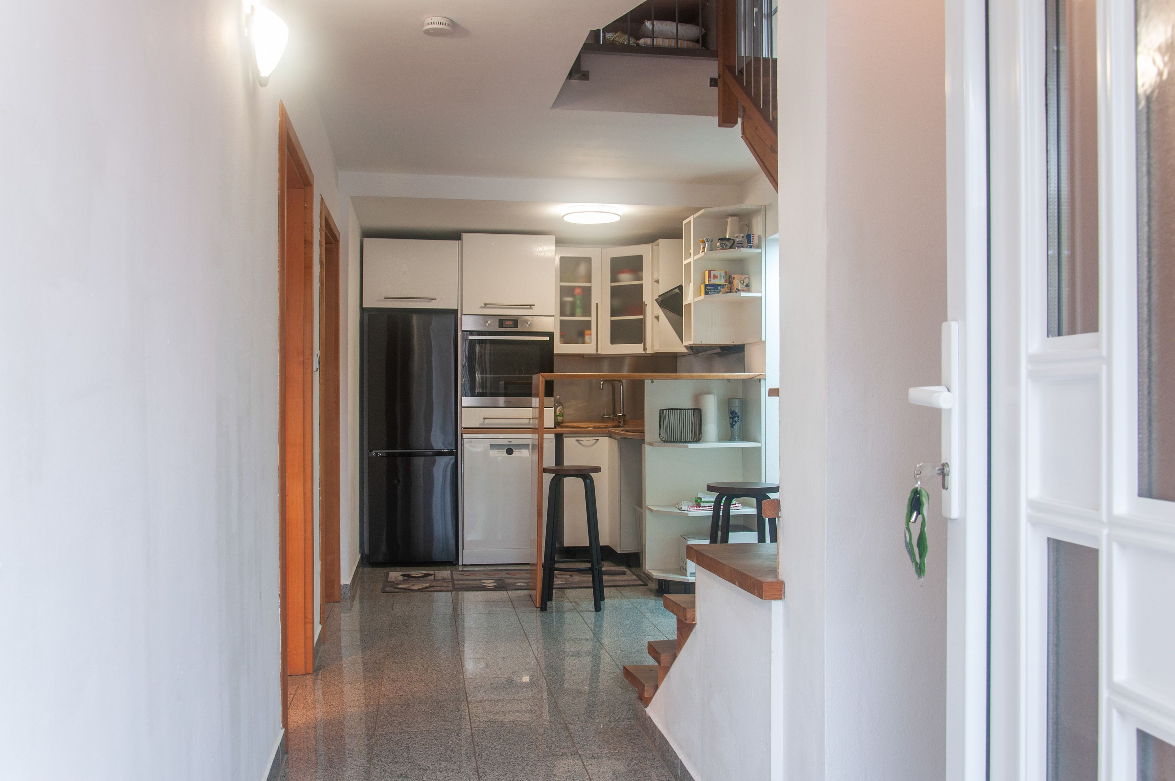 Un pasillo estrecho que conduce a una cocina con armarios blancos, un refrigerador de acero inoxidable y un horno empotrado.