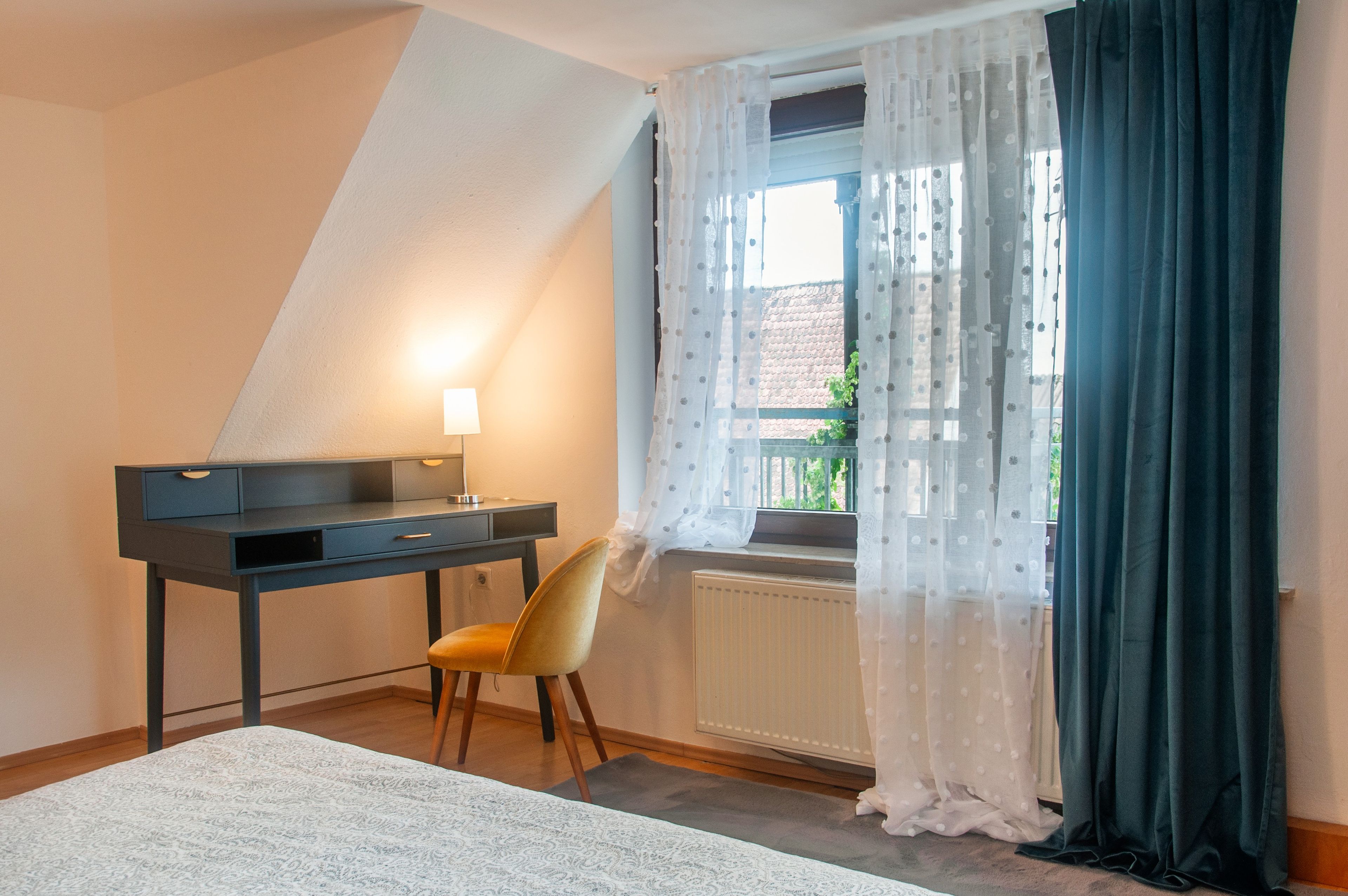 A bedroom with a desk, chair, and a window with curtains.
