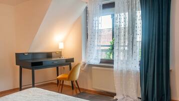 A bedroom with a desk, chair, and a window with curtains.