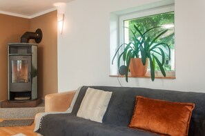 Uma sala de estar com sofá, lareira, janela com planta e luminária na parede.