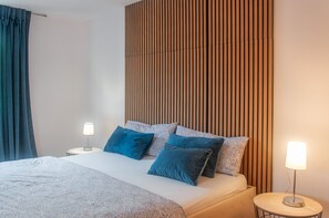 Quarto de hotel com uma cama, duas luminárias laterais e cabeceira de madeira.