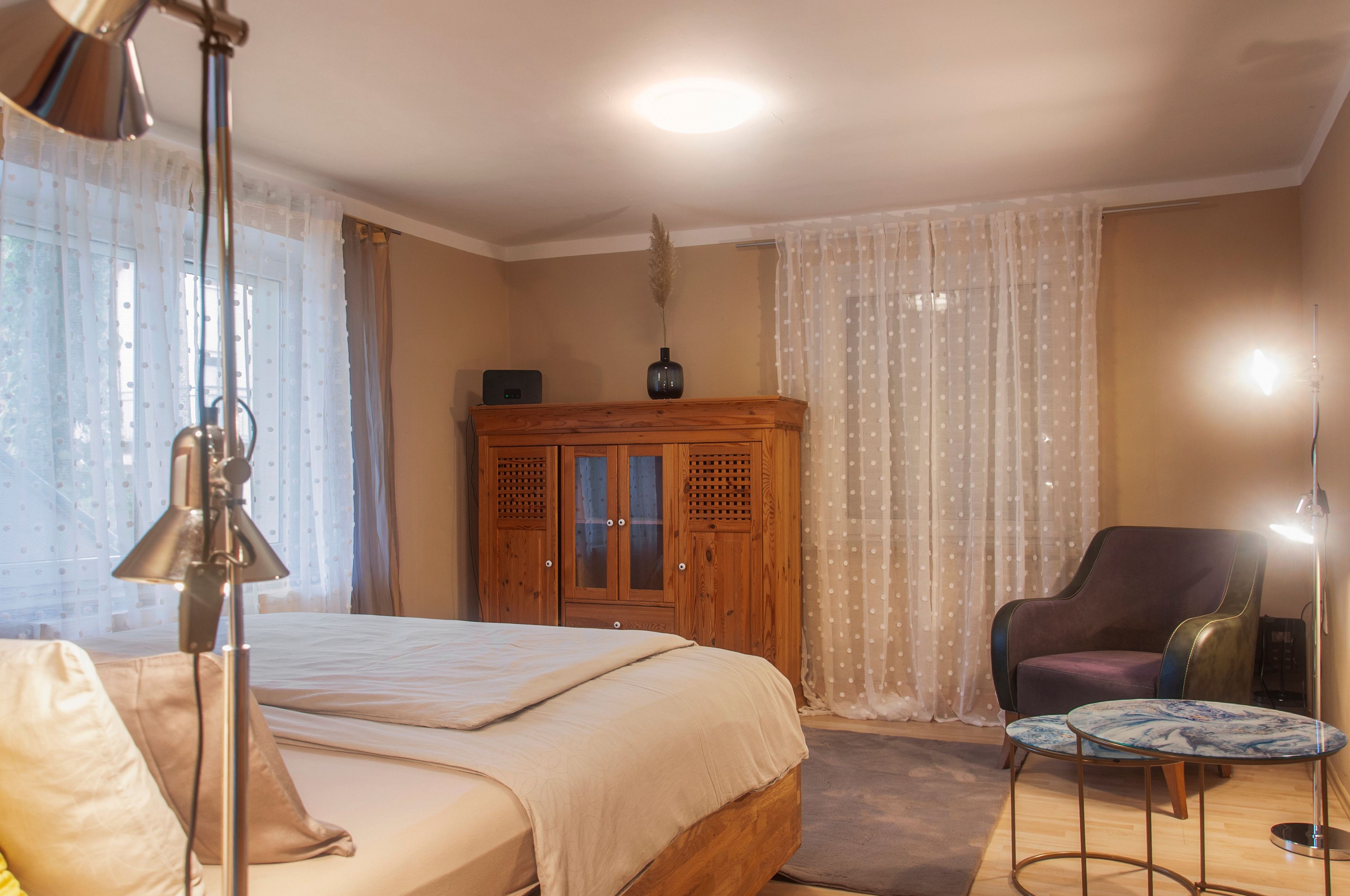 A bedroom with a bed, a wooden cabinet, a chair, and a small table.