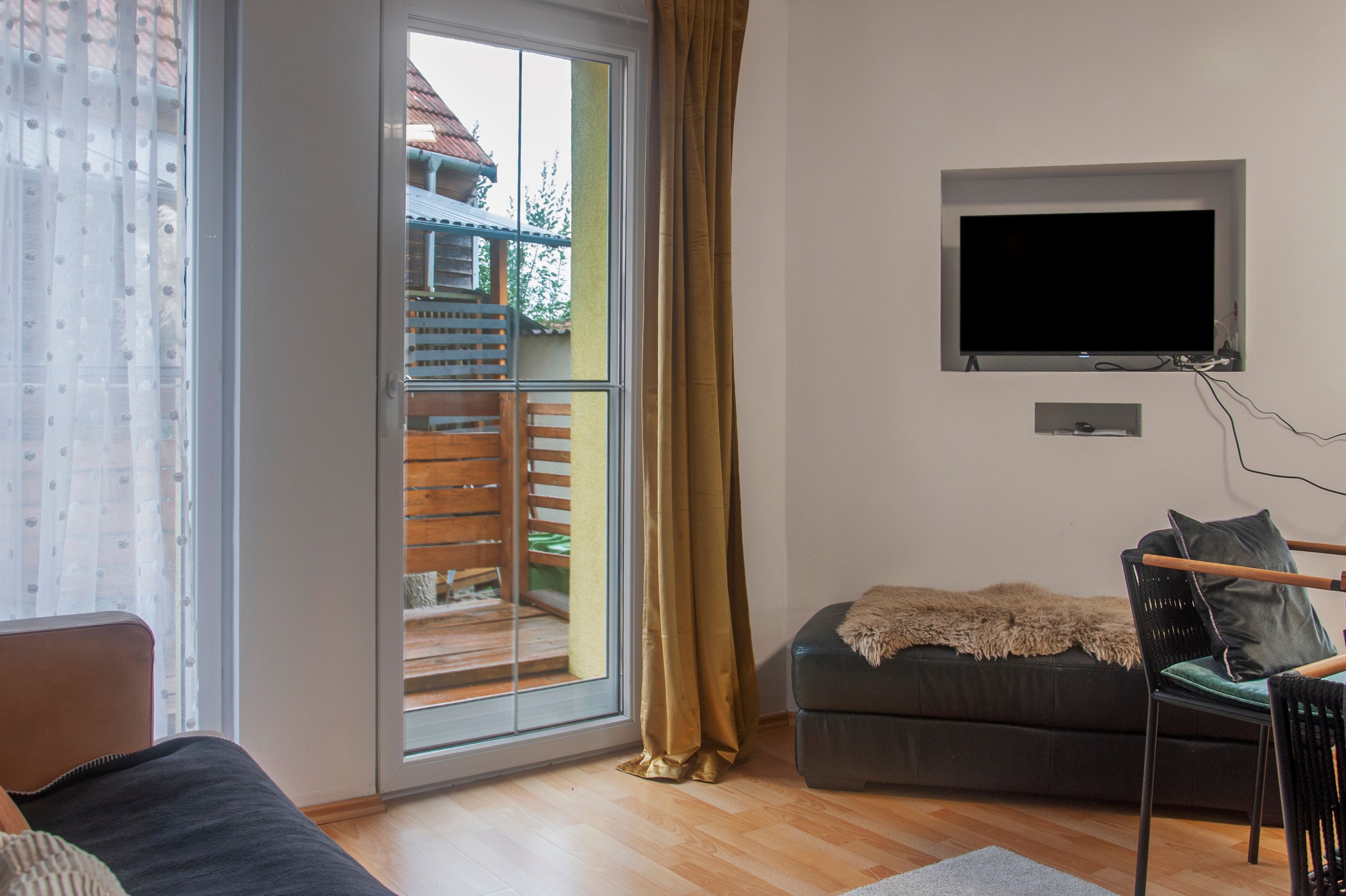 A living room with a sofa, a television mounted on the wall, and a sliding glass door leading to an outdoor area.