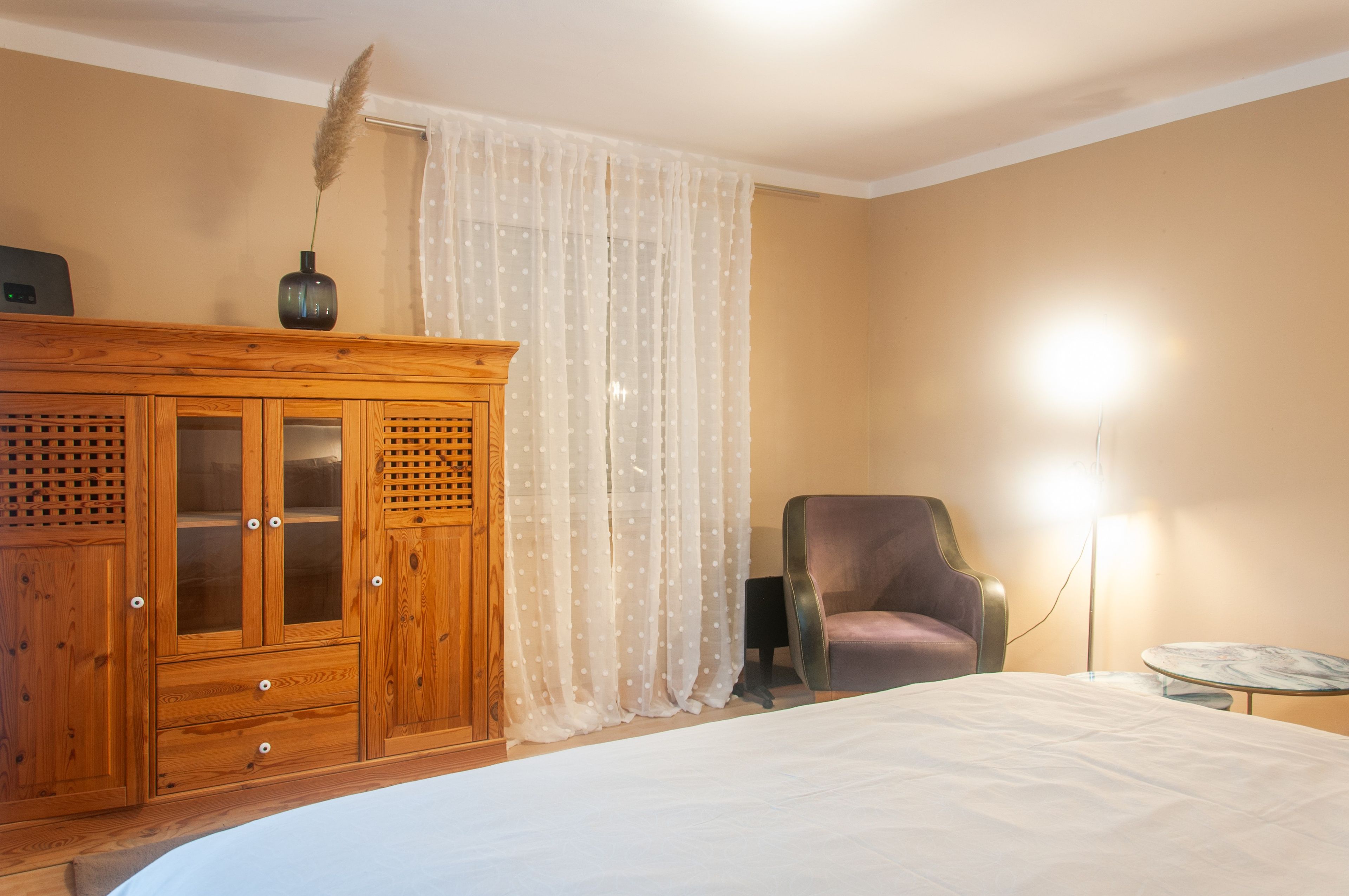 Une chambre à coucher avec une armoire en bois, une chaise, une table de chevet et une lampe.