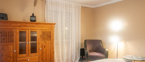 Un dormitorio con armario de madera, una silla, una mesita de noche y una lámpara.