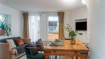 A modern living room with a wooden dining table, a sofa, and a TV mounted on the wall.