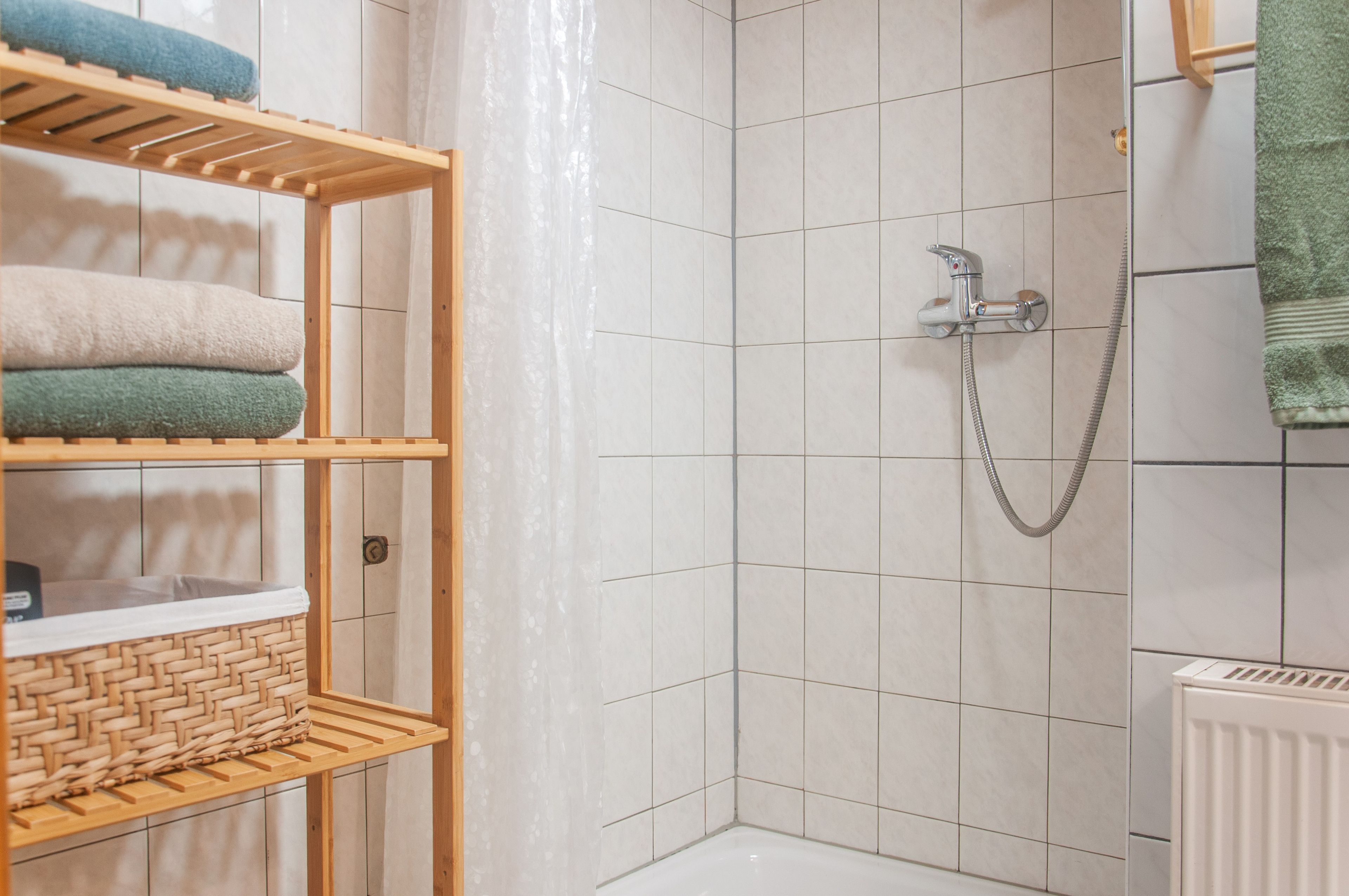 Un espace douche avec un mur carrelé, une pomme de douche et un porte-serviettes sur lequel sont pliés des serviettes.