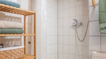 Un espace douche avec un mur carrelé, une pomme de douche et un porte-serviettes sur lequel sont pliés des serviettes.