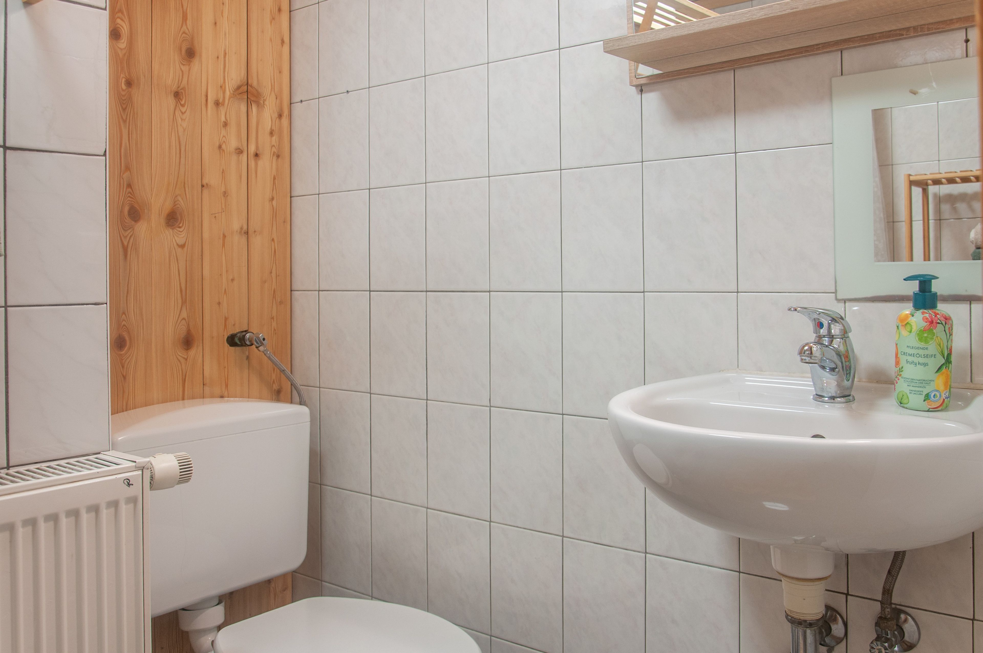 A bathroom with a white toilet, a white sink with a faucet, and a wooden panel above the toilet.
