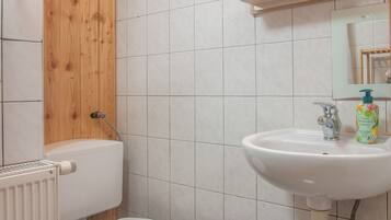 A bathroom with a white toilet, a white sink with a faucet, and a wooden panel above the toilet.