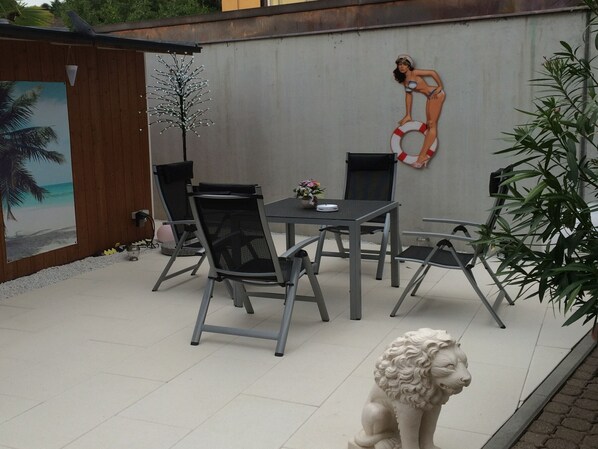 Une terrasse avec une table à manger, des chaises, une statue de lion décorative, une fresque murale et une plante en pot.