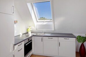 A modern kitchen with white cabinets, a built-in oven, a sink, and a skylight.