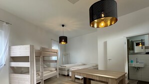 Une chambre moderne avec des lits superposés, une table en bois et une salle de bain équipée d’un lavabo et d’un miroir.