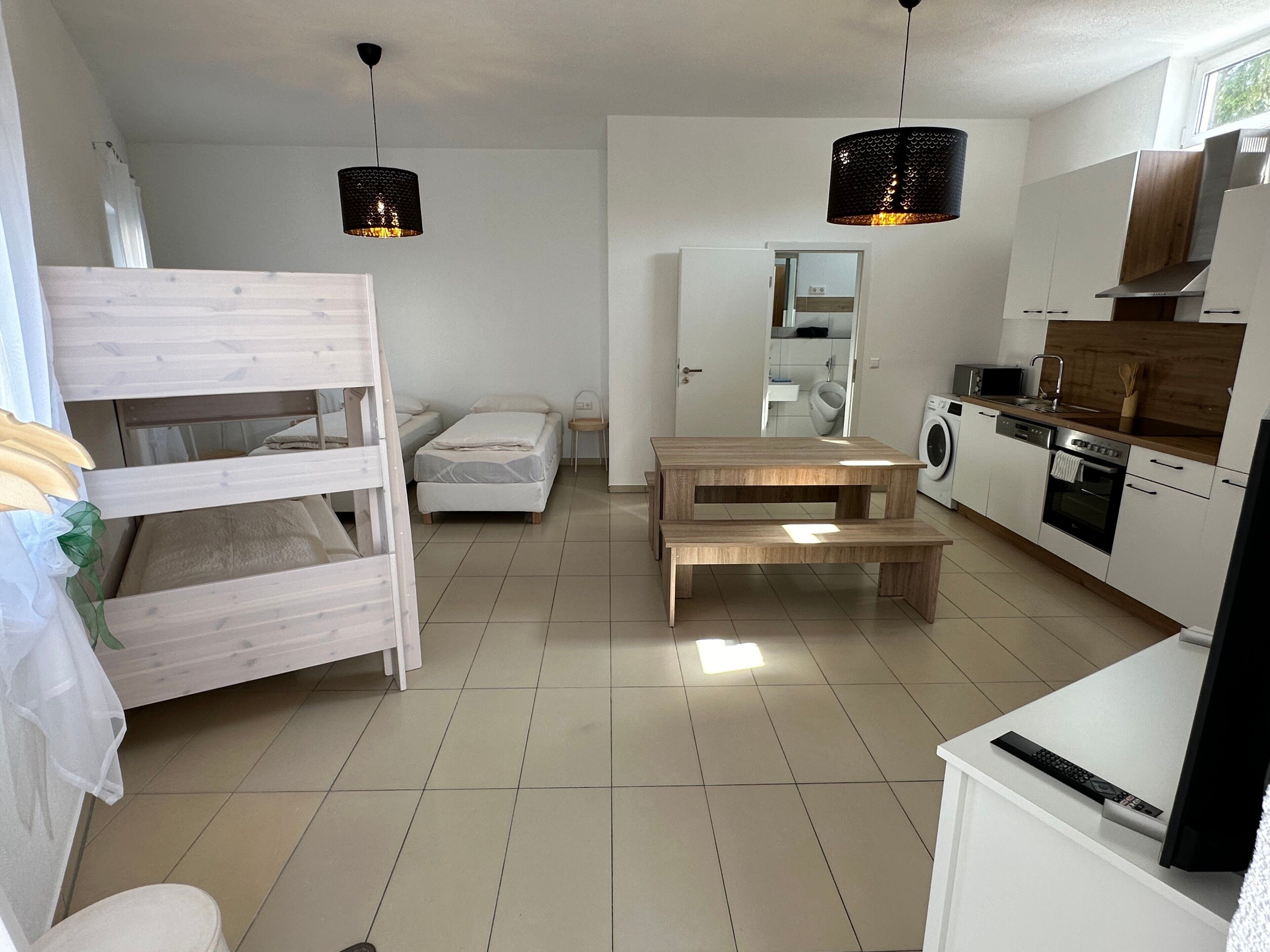 A compact living space with a bunk bed, a dining table, a kitchen area, and a washing machine.