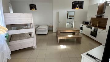 A compact living space with a bunk bed, a dining table, a kitchen area, and a washing machine.