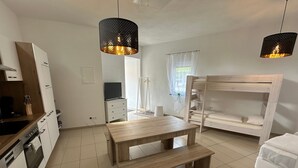 Une pièce compacte avec une table en bois, des lits superposés, un coin cuisine et des lampes suspendues.