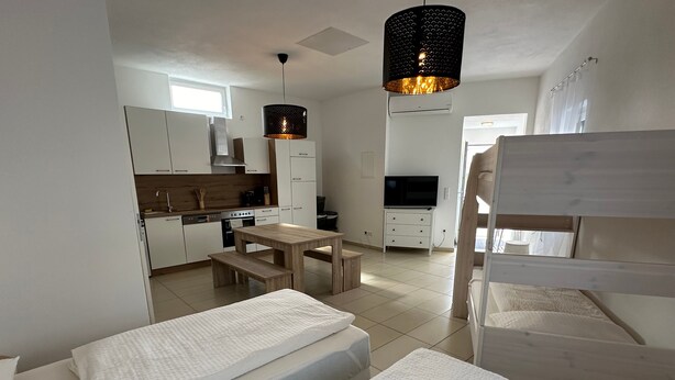 Une chambre de taille réduite comprenant deux lits, un coin cuisine, un espace repas et un téléviseur.