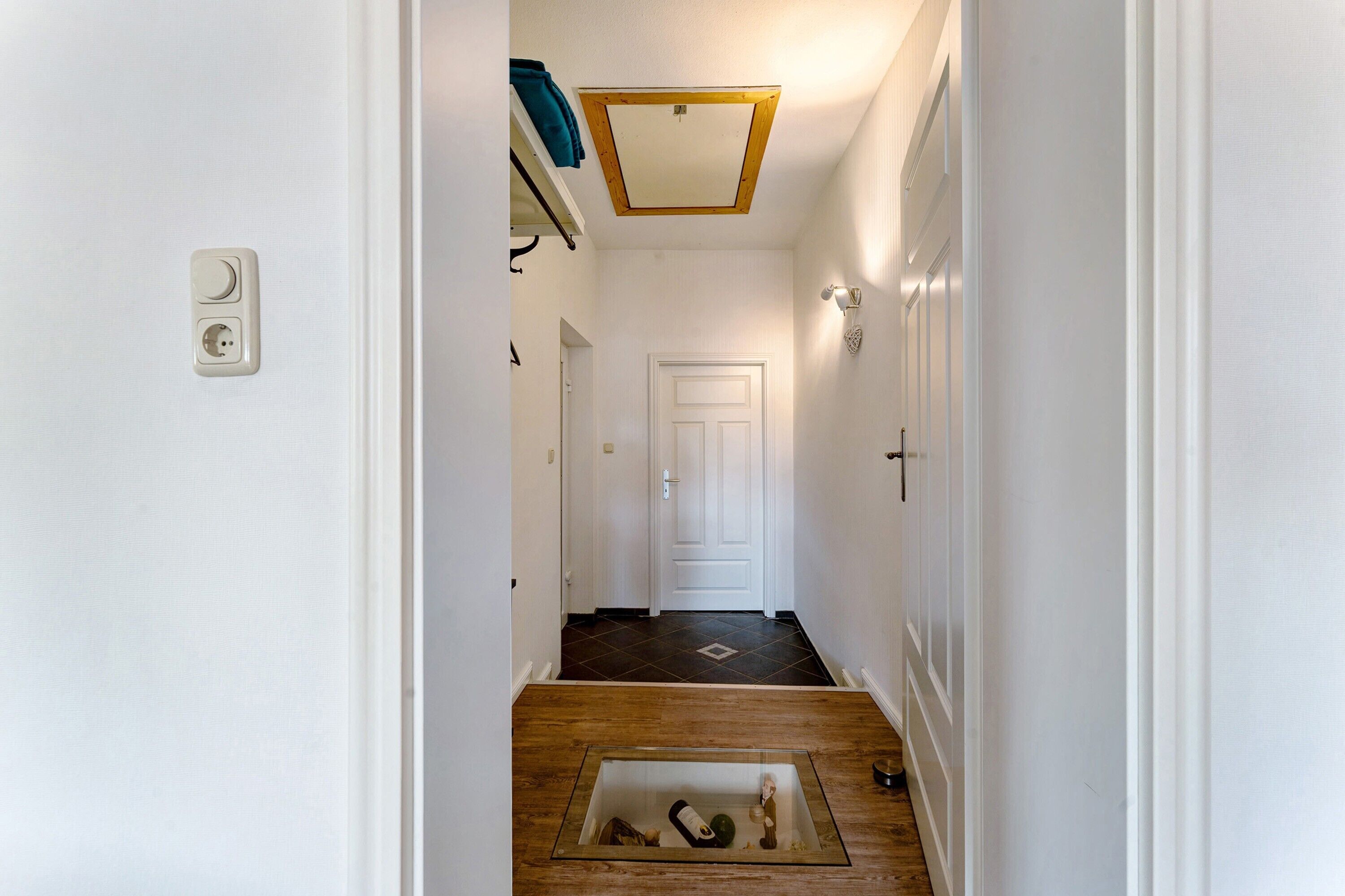 Un couloir étroit avec un plancher en bois, une porte blanche au fond et un luminaire au plafond.