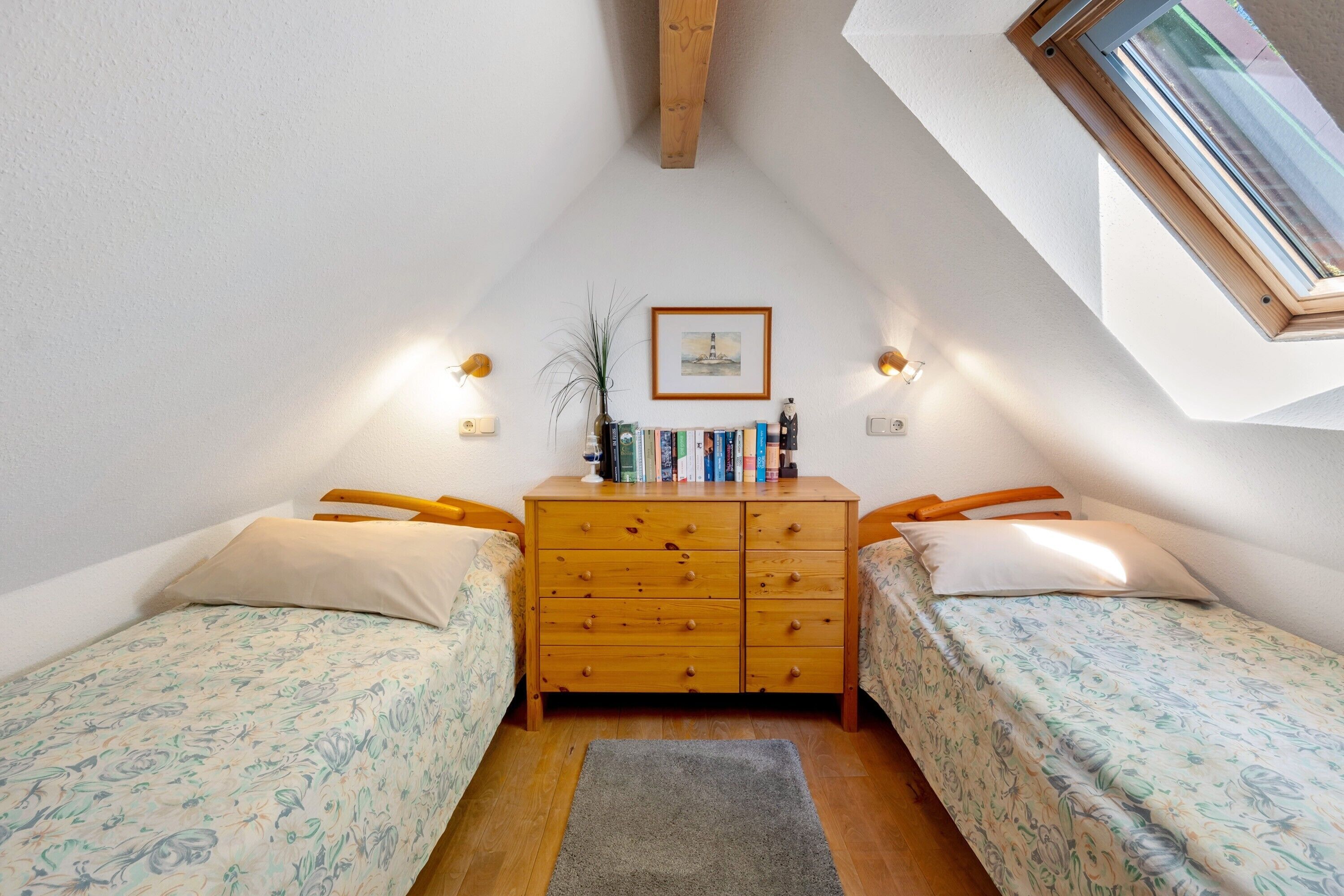 Un dormitorio con dos camas individuales, un aparador de madera, un tragaluz e imagen enmarcada en la pared.