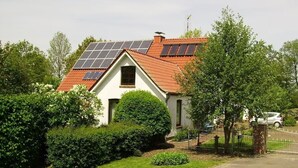A house with solar panels on the roof, surrounded by greenery.