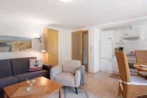 Olohuoneessa on sohva, nojatuoli ja sohvapöytä, ruokailutilassa pöytä ja tuolit sekä keittiössä kaappeja ja kodinkoneita.