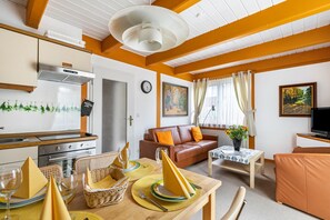 Ein möbliertes Wohnzimmer mit einer Couch, einem Esstisch gedeckt mit gelben Servietten, einem Fernseher und einer Küchenzeile mit Herd und Schränken.
