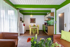 A living room with a sofa, a dining table with chairs, a kitchen area, and a door. - Apartment 'Atlanta  101' with Private Terrace, Private Garden and Wi-Fi (Pellworm)