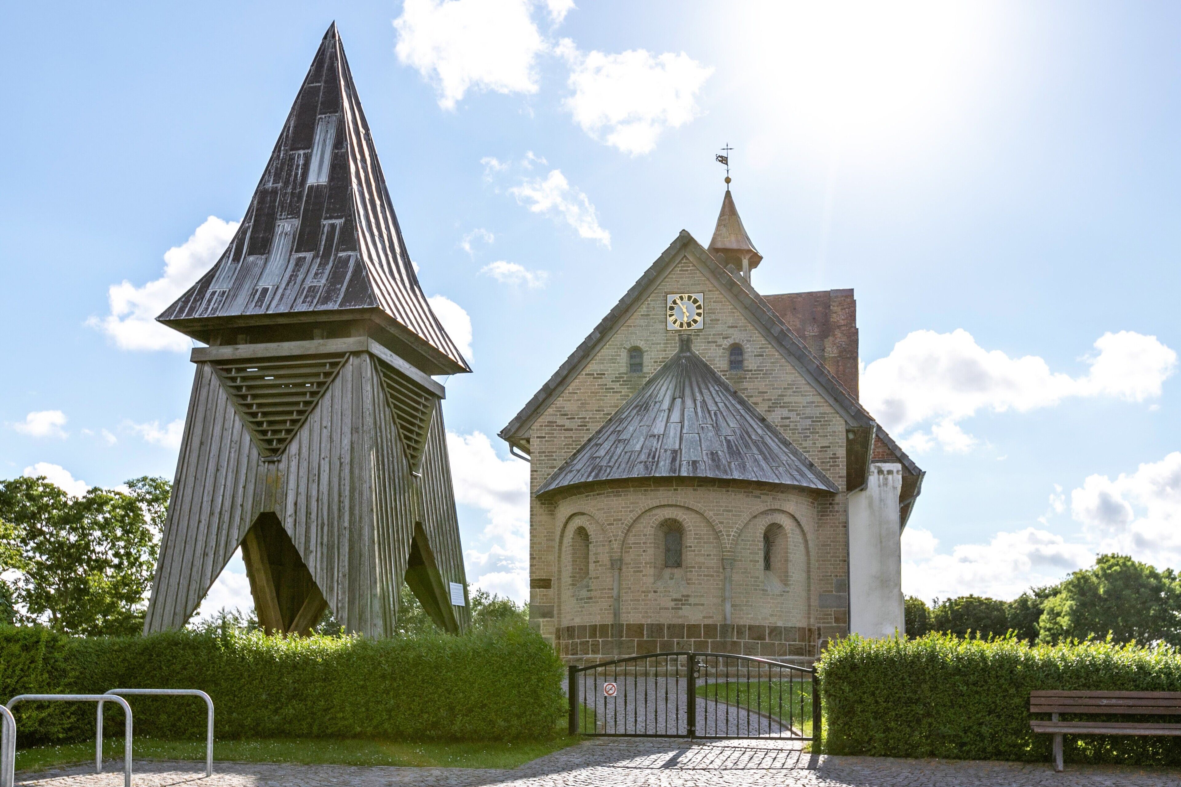 A church with a clock tower and a modern structure with a pointed roof.