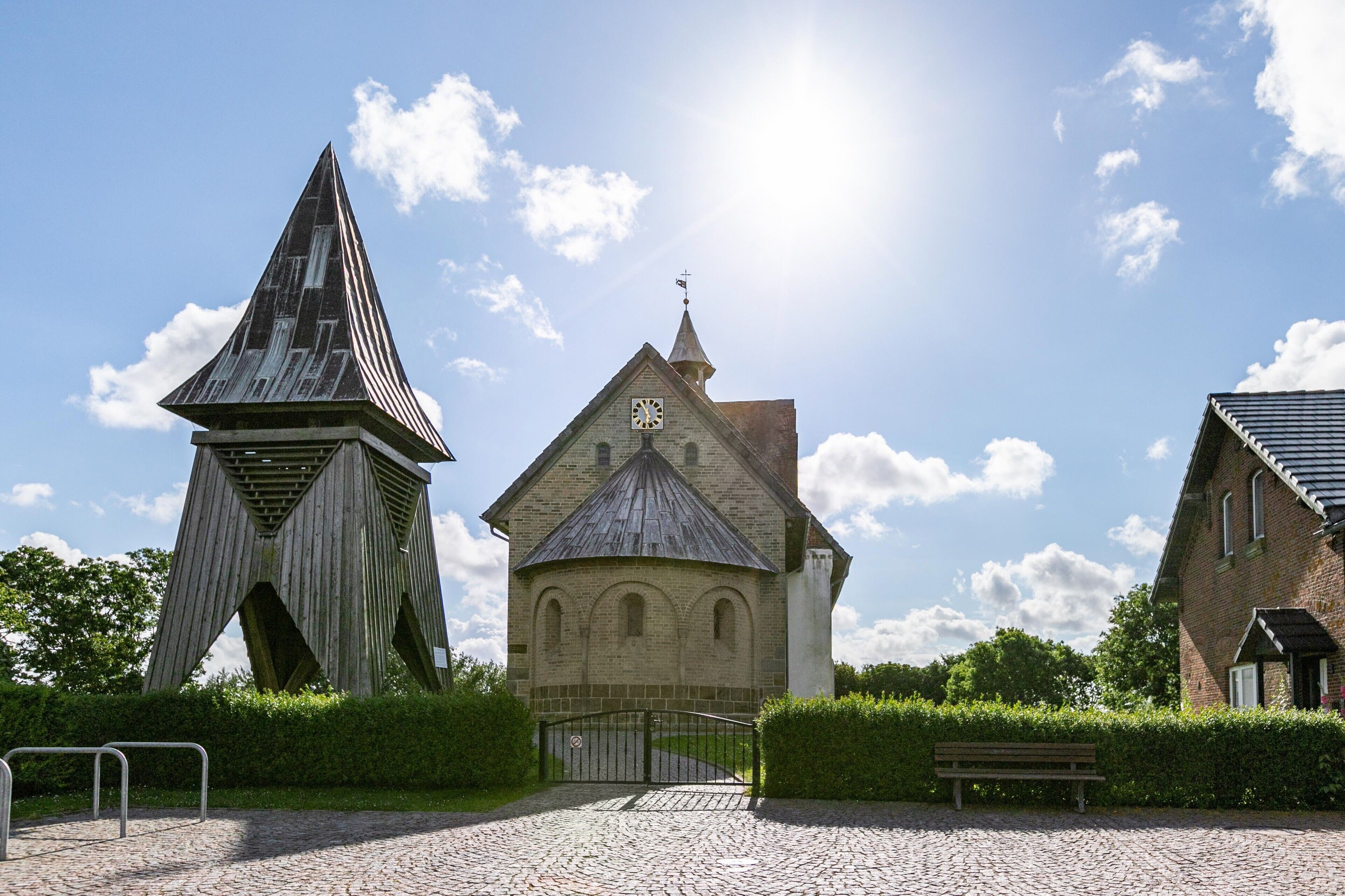 Eine Kirche mit einem Glockenturm, einem Kopfsteinpflasterweg und einer Bank.