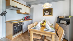 Una cocina moderna con armarios de madera, horno empotrado, mesa de comedor con sillas y una lámpara colgante.