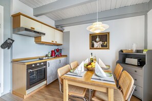 A modern kitchen with wooden cabinets, a built-in oven, a dining table with chairs, and a hanging light fixture.