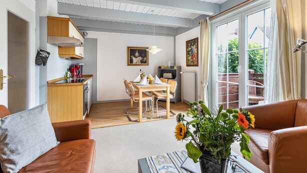 Una sala de estar con un sofá, un comedor con mesa y sillas, una zona de cocina y vistas al exterior a través de un ventanal.