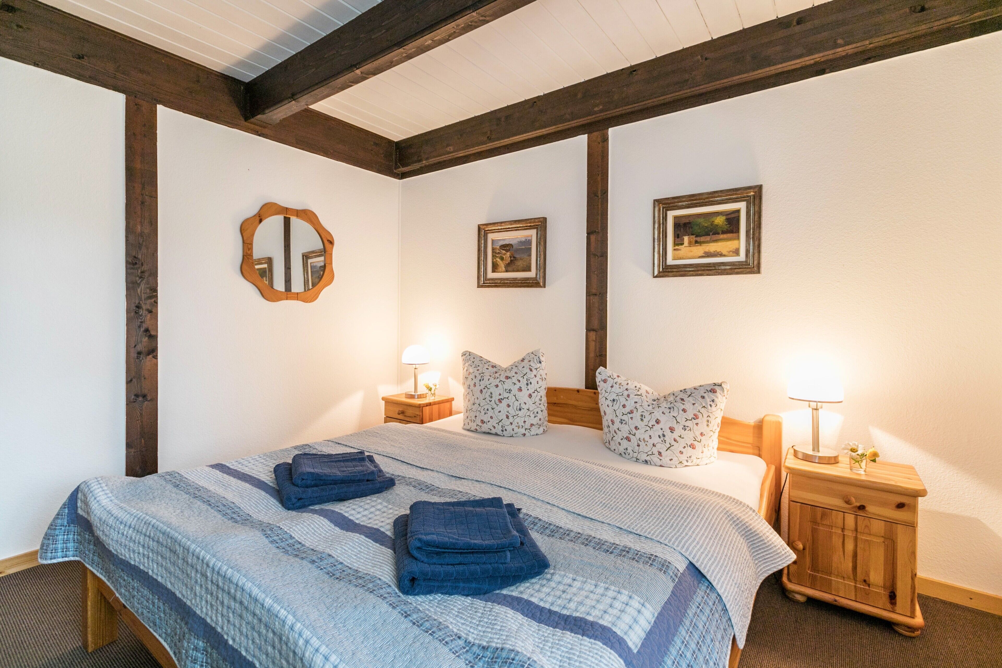 A bedroom with a bed, two nightstands, a mirror, and two framed pictures on the wall.